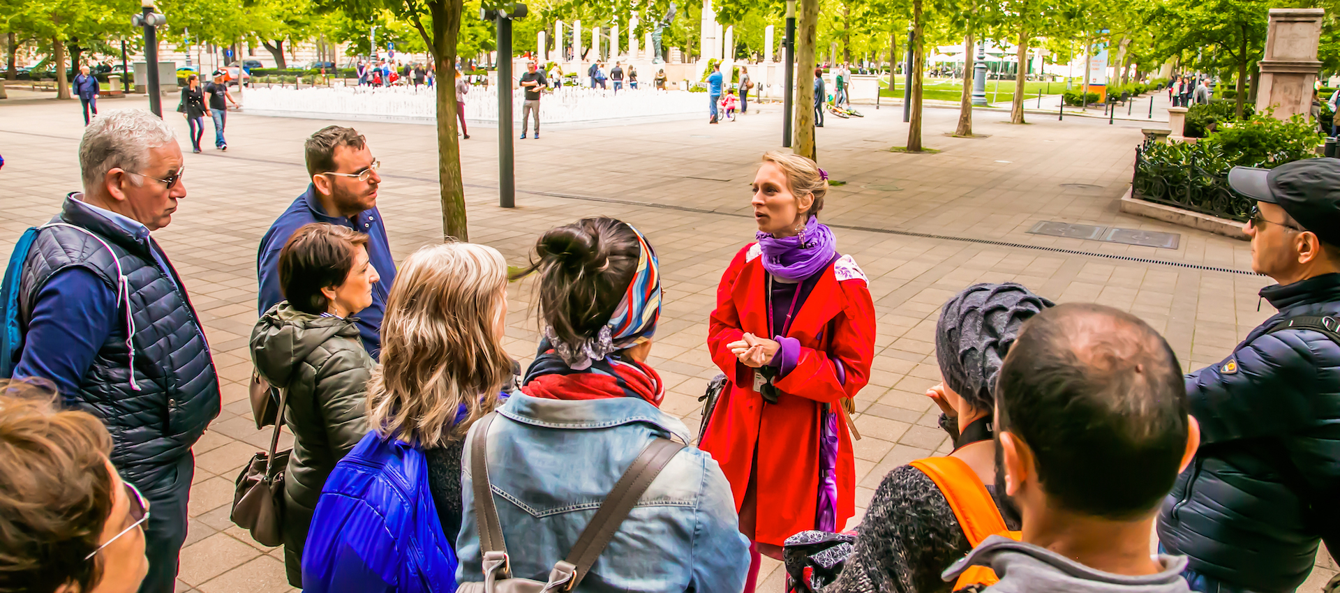 Eine Frau steht vor einer gemischten Gruppe Personen in einer Fußgängerzone und erklärt etwas.